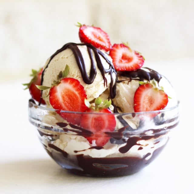 Bowl of vanilla ice cream topped with fresh strawberries and chocolate fudge sauce.