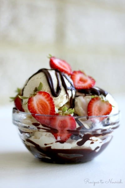 Bowl of vanilla ice cream topped with fresh strawberries and chocolate fudge sauce.
