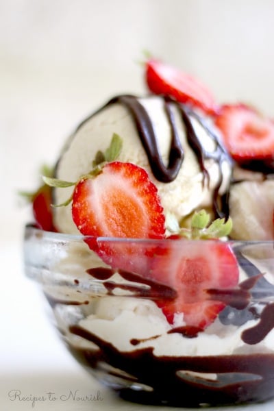 Bowl of vanilla ice cream topped with fresh strawberries and chocolate fudge sauce.