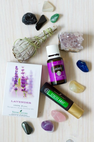 Dried sage smudge bundle, Young Living lavender essential oil and Stress Away essential oil roll-on bottle, and lots of crystals like rose quartz and amethyst.