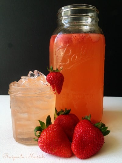 Strawberry switchel in a half gallon mason jar and over ice in a mall jar with fresh strawberries.