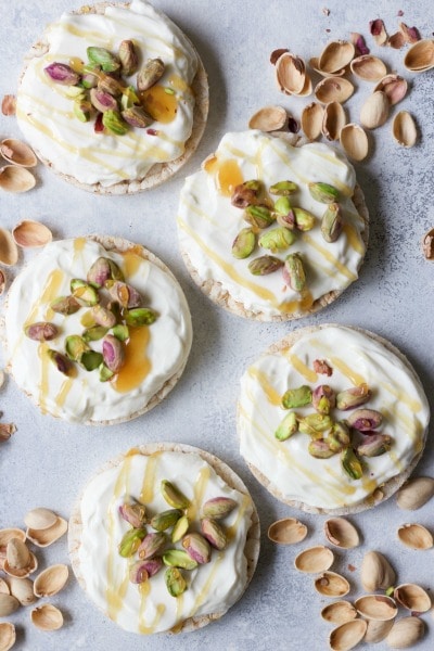 Rice cakes topped with cream cheese, pistachios and honey next to pistachio shells. 