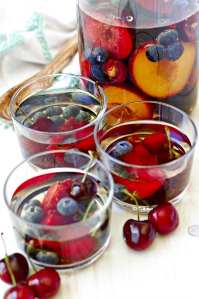 Glasses and a pitcher of sangria with cherries, blueberries, plums and peaches.