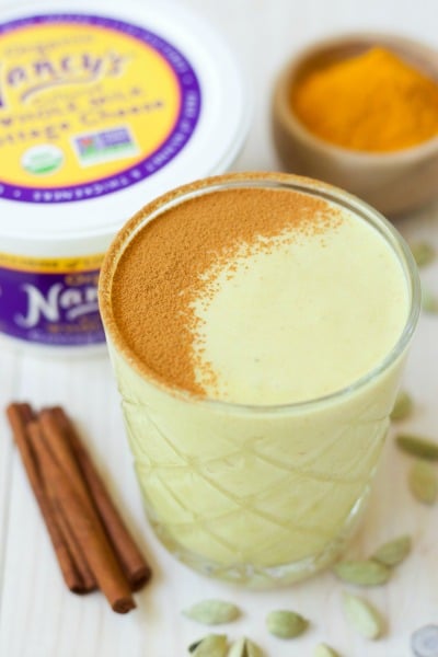 Glass of golden milk smoothie, bowl of ground turmeric, cinnamon sticks and container of Nancy's organic whole milk cottage cheese.