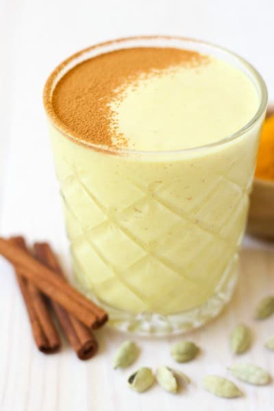Glass of golden milk smoothie with ground cinnamon on the top.