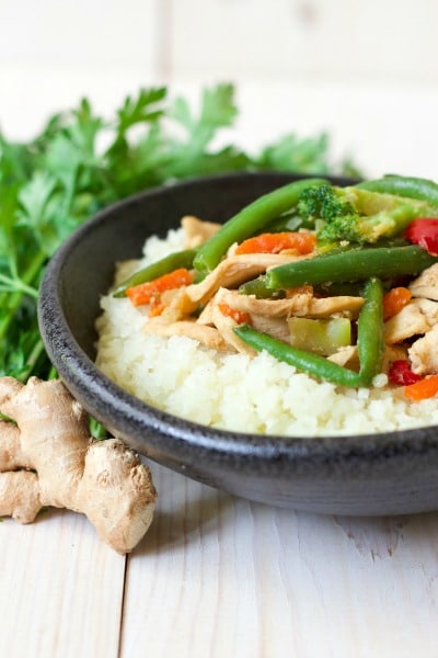 Bowl of vegetable chicken stir fry over cauliflower rice with fresh herbs and ginger.
