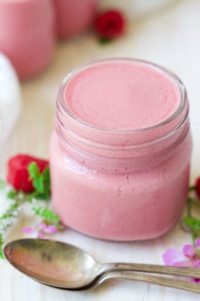 Jar of pink raspberry smoothie next to fresh raspberries and flowers.