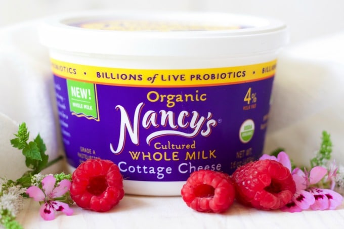 Container of Nancy's organic whole milk cottage cheese with fresh raspberries and flowers.