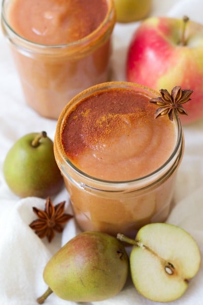 Jars of homemade applesauce dusted with cinnamon and surrounded by whole pears, apples and star anise.