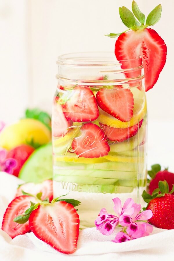 Mason jars filled with water, strawberries, lemon slices and cucumber slices.