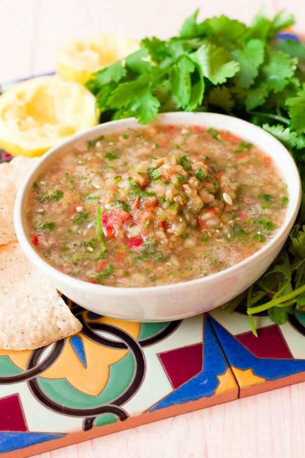 Large bowl of chunky blender salsa surrounded by chips, cilantro and juiced lemons.