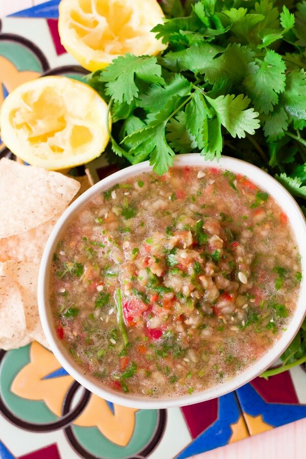 Large bowl of chunky blender salsa surrounded by chips, cilantro and juiced lemons.