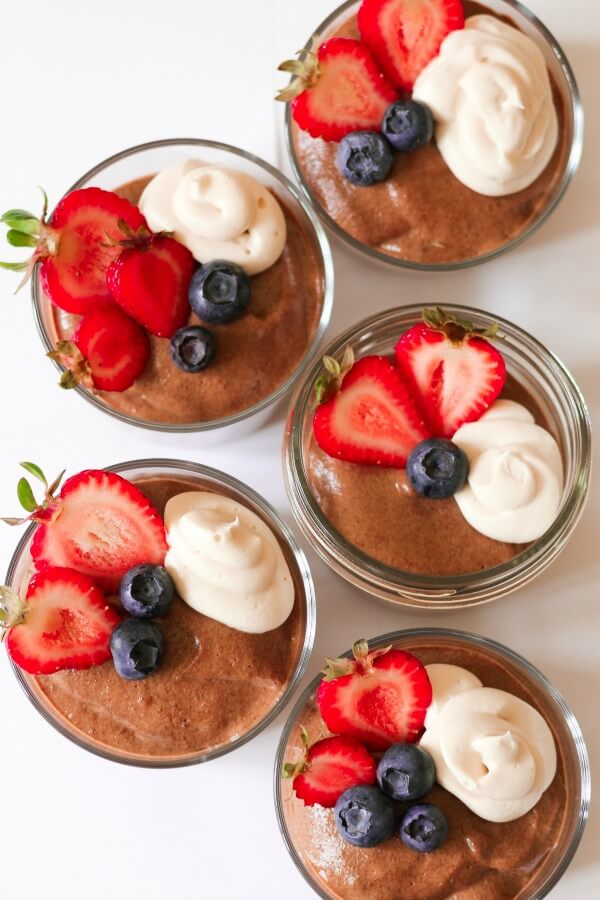 Jar of smooth chocolate chia pudding with berries and cream on the top.