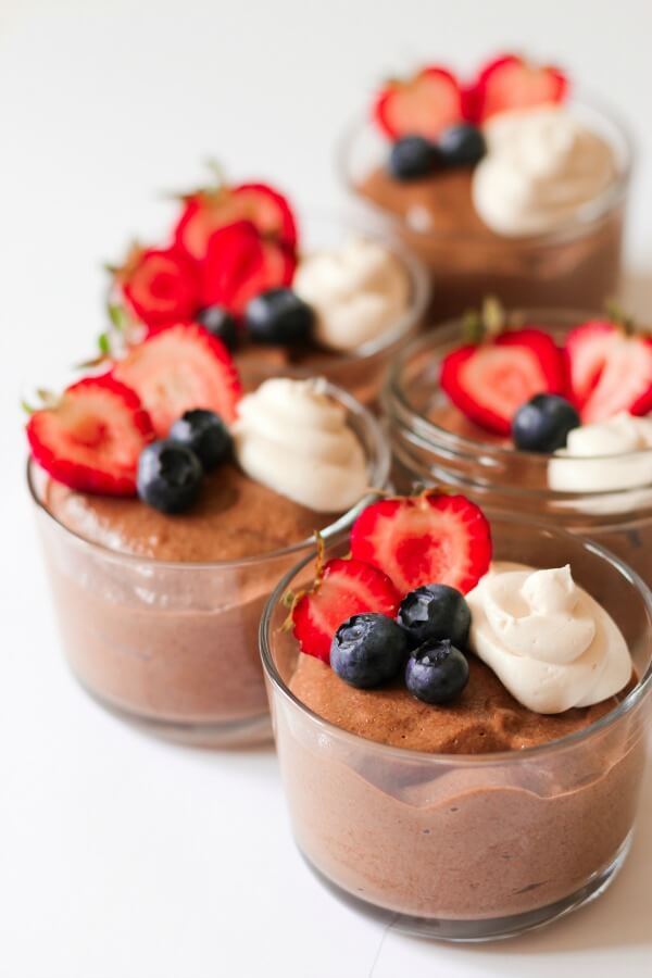 Jars with smooth chocolate chia pudding with berries and cream on the top.