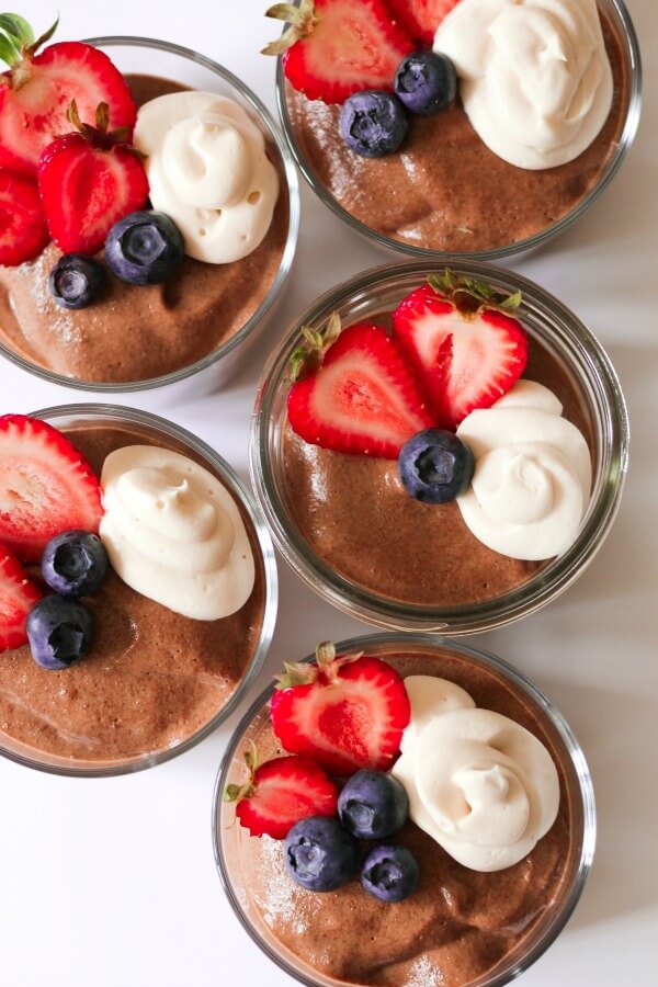 Jars of smooth chocolate chia pudding with fresh berries and cream on the top.