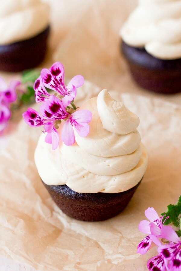 Vanilla buttercream frosting swirled on top of chocolate cupcakes with pink flowers.