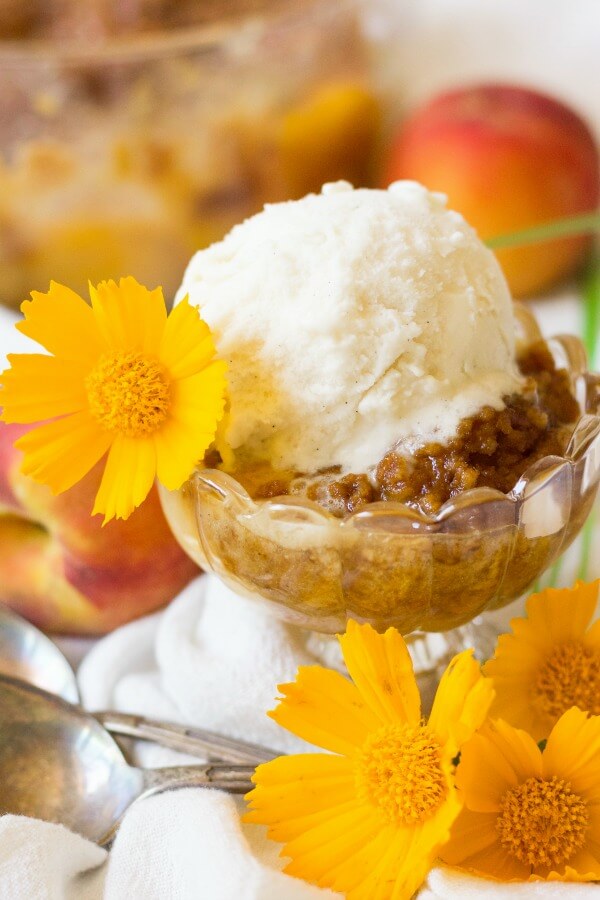 Scoop of vanilla ice cream on top of peach crumble with fresh peaches.