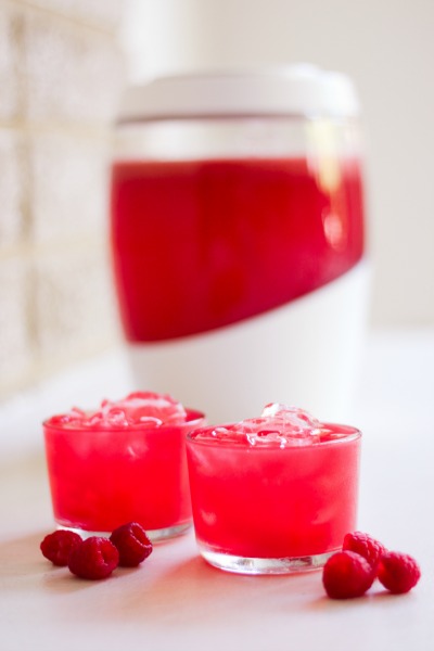 Glasses with pink raspberry soda, fresh raspberries and a fermenting crock.