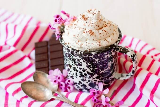 Mug full of whipped cream with chocolate shaved over the top and chocolate on the side.