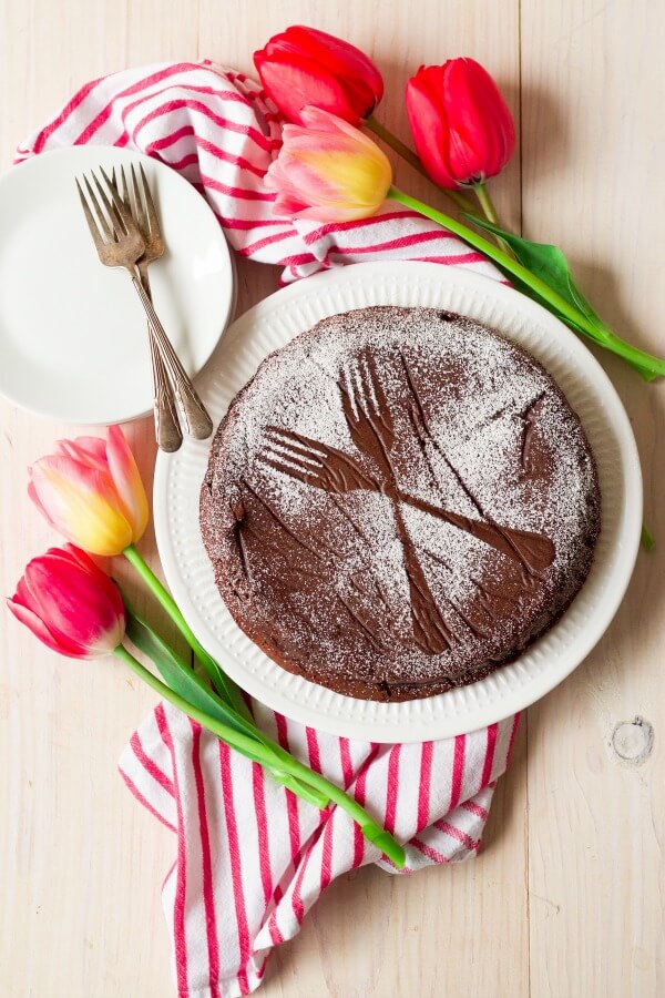 Chocolate torte cake dusted with powdered sugar making two forks sample next to tulips.