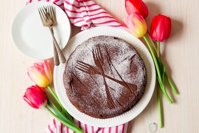 Chocolate torte cake dusted with powdered sugar making two forks sample next to tulips.